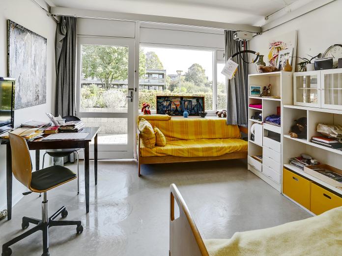 Lyst værelse med stort vinduesparti og dør ud til terrasse. Værelset er indrettet med loftslift og plejeseng samt personlige møbler som sofa, bord og stole samt en reol.