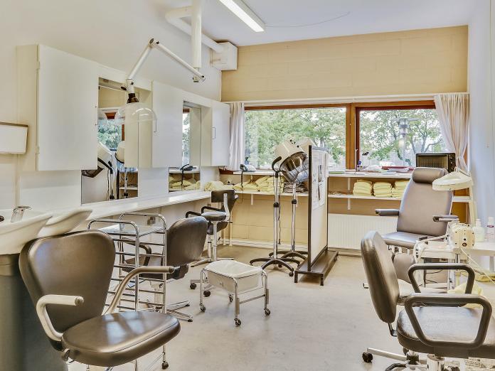 Frisørsalon med stole, station til hårvask og tørrehjelme. Her er også plads til fodterapi med en fodterapeutstol og et fodbad på hjul. 