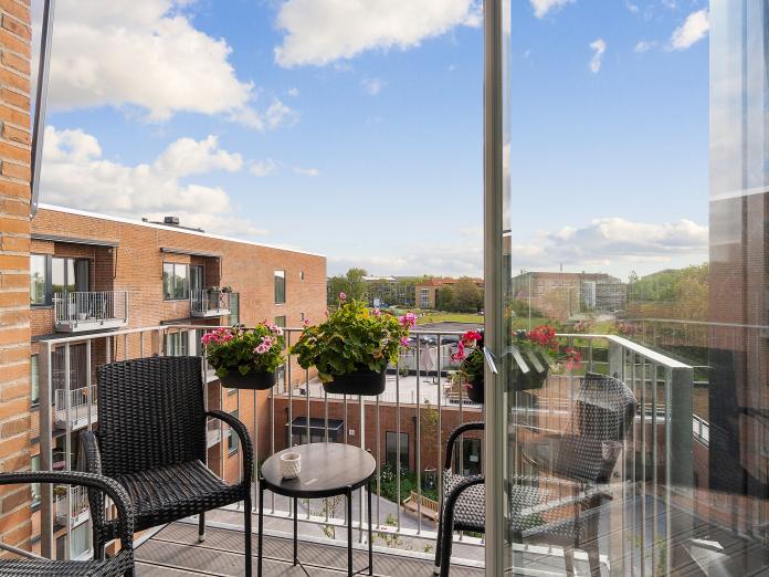 Privat altan med kurvemøbler og konsolbord samt altankasser med blomster. 