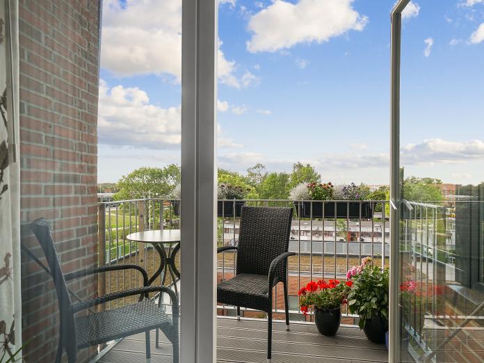 Privat altan med to kurvemøbler, et cafébord samt blomster i krukker og altankasser.