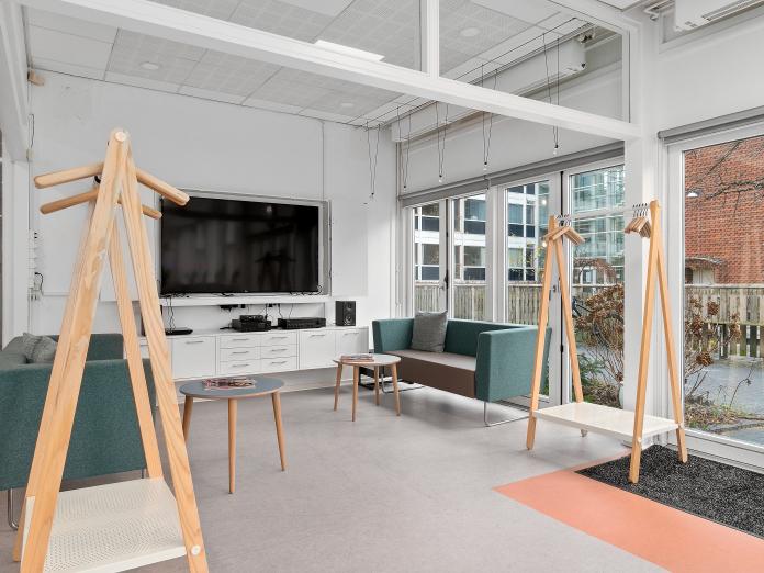 Hyggekrog i hjørne af fællesrum indrettet med sofaer, sofaborde, stort fjernsyn og garderobestænger.