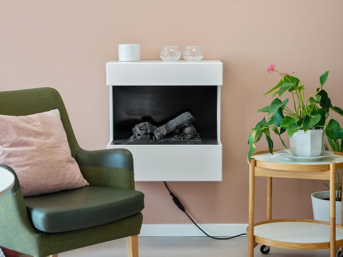 Hyggekrog med elektrisk pejs, grøn læsestol og bakkebord med en potteplante.