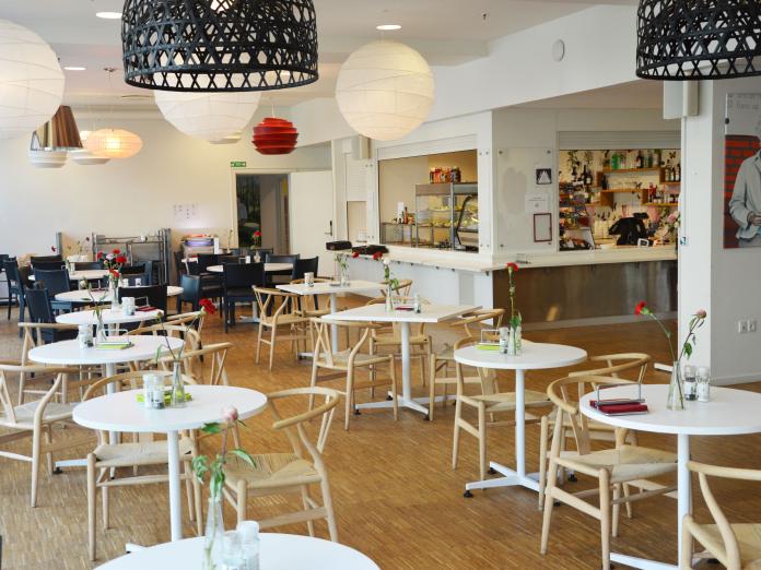 Fælles caféområde med stole omkring caféborde samt en café, hvor der kan købes mad og drikke.
