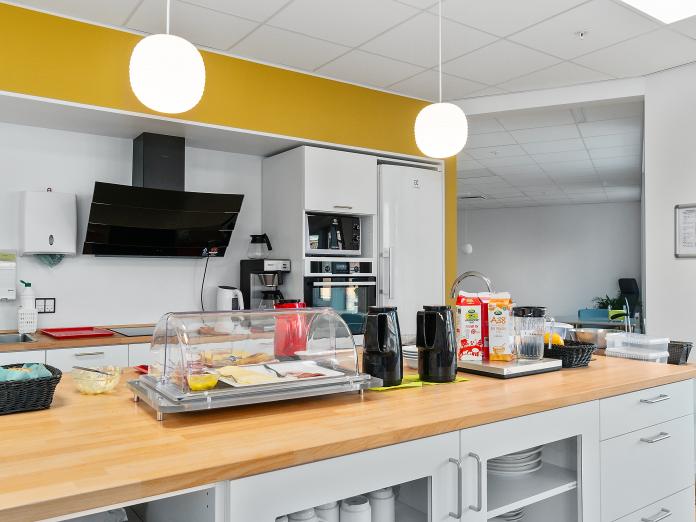 Stort åbent køkken, hvor morgenmad som yoghurt, pålæg og kaffe er stillet frem på disk.