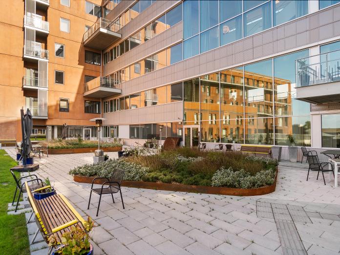 Fliseterrasse med bede med grønt og urter samt bænke, havemøbler, parasoller og terrassevarmer.