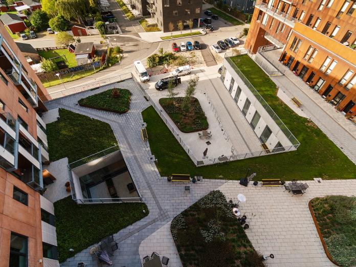 Gårdhave set ovenfra. Haven er indrette med flisegangstier og -terrasser samt græs, grønne bede og træer.