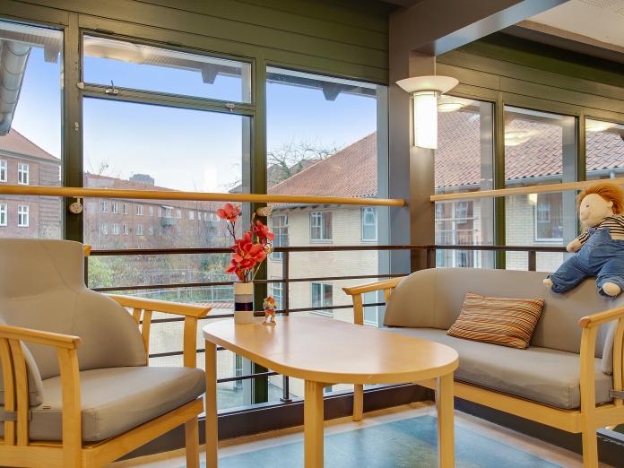 Sofahjørne foran store vinduespartier indrettet med sofa, lænestol og sofabord.