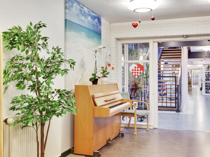 Hjørne med klaver, stor, grøn plante og blomster. På væggen hænger et billede fra en sandstrand.