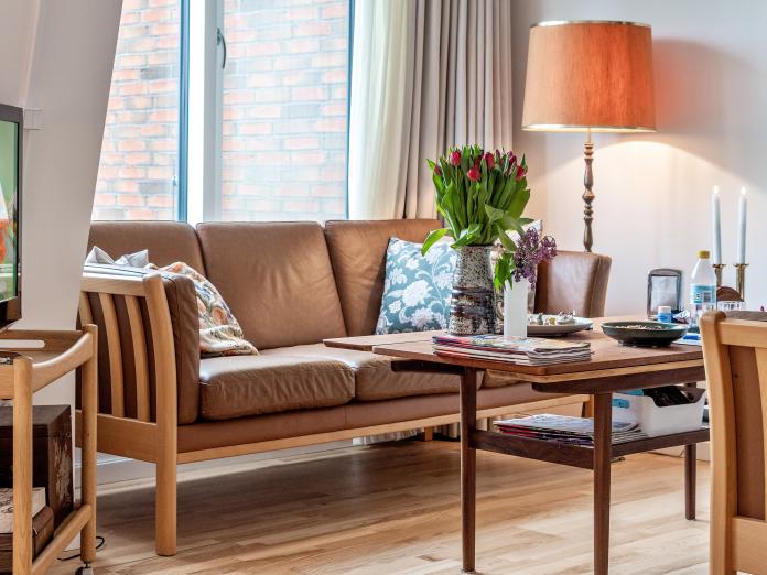 Hjørne af værelse med sofa, sofabord med blomster og nips samt standerlampe og fjernsyn.