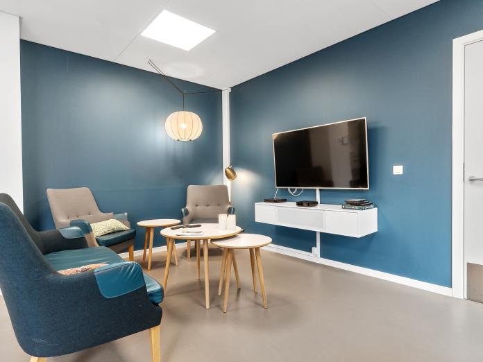 Hyggekrog med blå vægge og sofagruppe med sofa, lænestole og borde foran et væghængt fjernsyn.