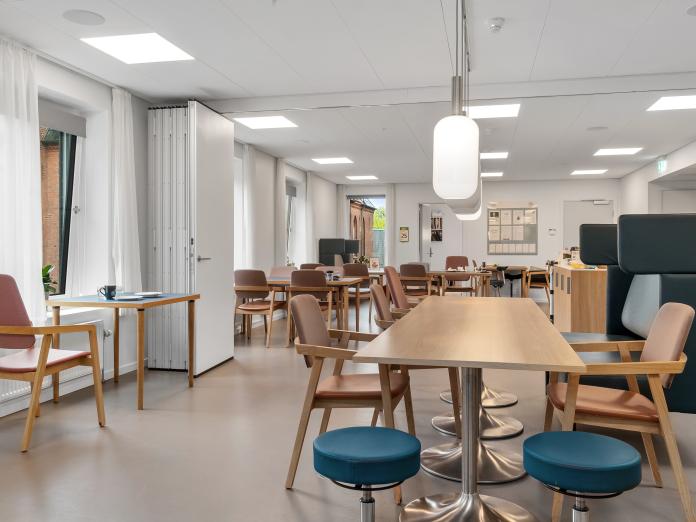 Aflangt fællesrum, der kan opdeles med foldedør. Rummet er indrettet med borde og stole samt en akustiksofa.