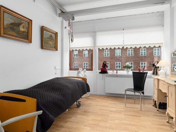 Soveværelse med store vinduespartierm loftslift og plejeseng. Værelset er desuden møbleret med personlige møbler og malerier på væggene. 