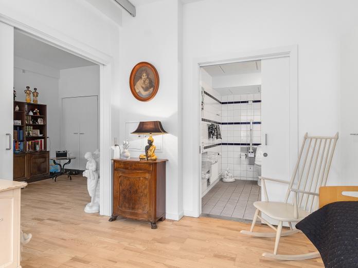 Lyst soveværelse med loftslift, plejeseng og personlige møbler. Fra soveværelset er der adgang til stue og til badeværelse.