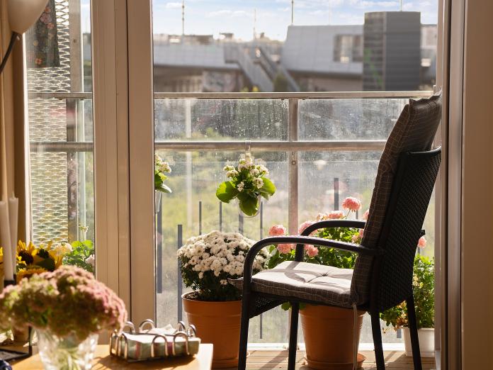 Åben dør ud til altan med kurvestol og mange krukker med blomster.