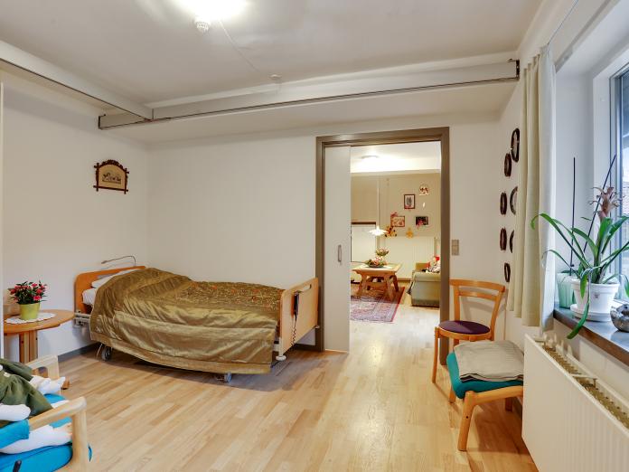 Lyst soveværelse med hospitalsseng, loftslift og personlige møbler.