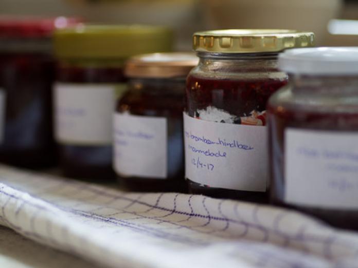 Nærbillede af hjemmelavede marmelader i glas på et ternet viskestykke. 