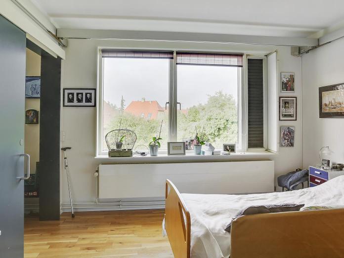 Soveværelse med skydelåge ind til stuen, plejeseng og to vinduer. 
