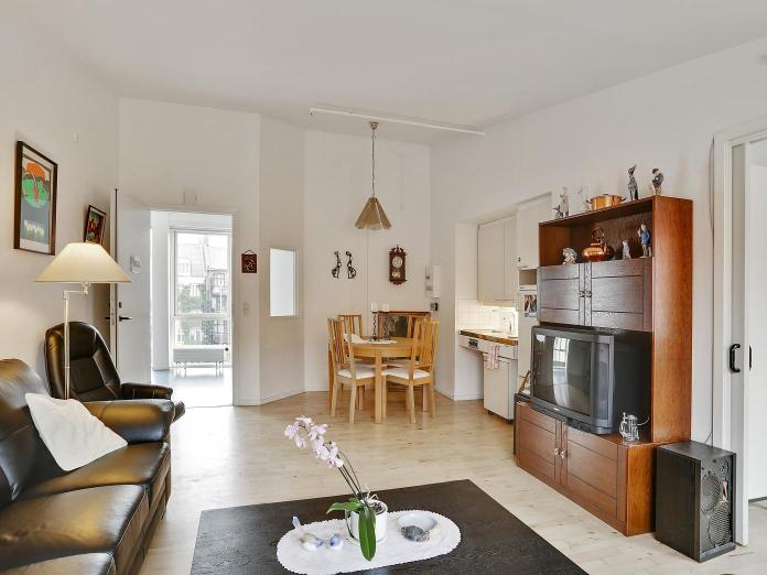 Stue med lille tekøkken, et lille rundt bord med fire spisebordsstole, sofa, lænestol, sofabord og tv-møbel.