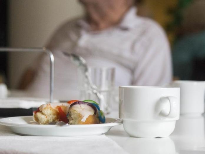 Nærbillede af kagetallerken med kage og en kaffekop samt i baggrunden en ældre person.