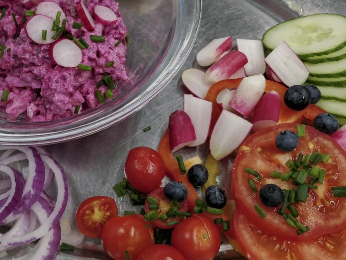 Fad med udskåret, rå grøntsager, som tomater, agurk, radiser og rødløg.