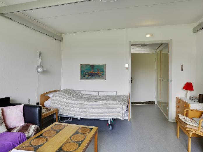 Lyst værelse med seng, loftslift og personlige møbler. Fra værelse er der en gang ud til fællesområderne, hvor der er indbyggede skabe.