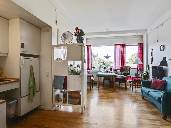 Lys stue med hvidt tekøkken med vask og køleskab. Stuen er indrettet med personlige møbler som sofa og spisebord med stole omkring.