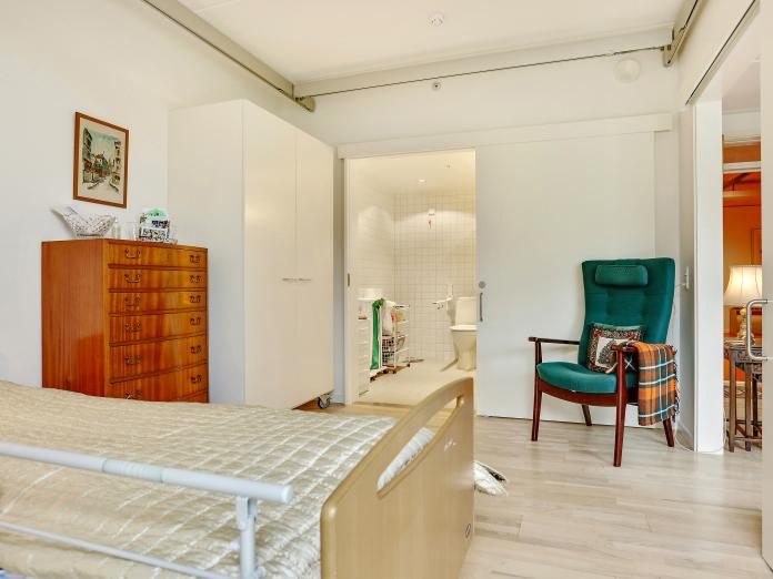 Soveværelse med hvide vægge og hvidt loft, loftslift, indbygget skab, seng samt personlige møbler. Der er skydedør mellem stue og soveværelse samt mellem soveværelse og badeværelse.