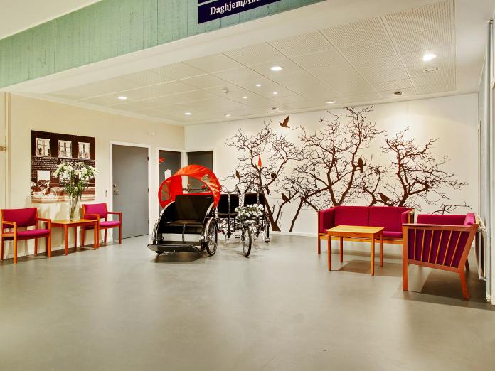 Hyggekrog med sofaer, stole og sofaborde. På endevæggen er en fotostat af et træ med fugle og foran væggen står to cykler parkeret.