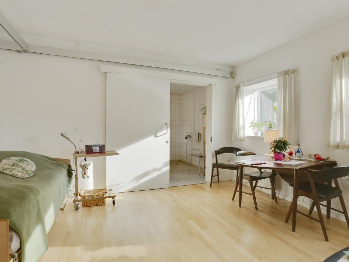 Lyst værelse med plejeseng og loftslift samt personlige møbler. Fra værelset er der adgang til et badeværelse gennem en skydedør.