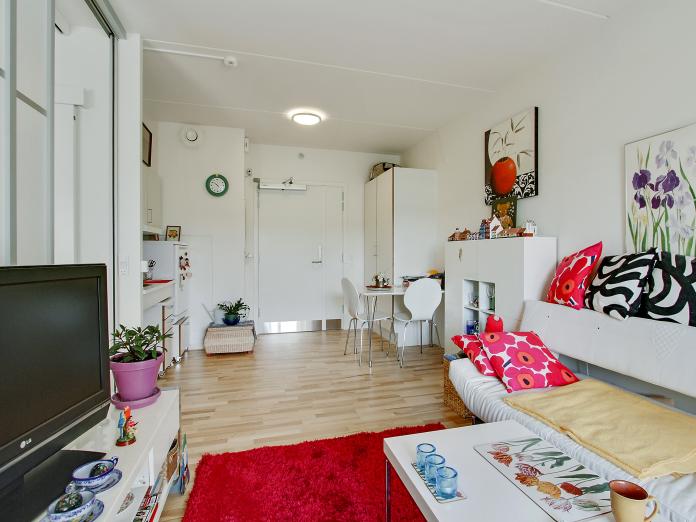 Lyst værelse med tekøkken og indbygget skab. Værelset er indrettet med personlige møbler som sofa, fjernsyn, reolsystem og et spisebord med stole.