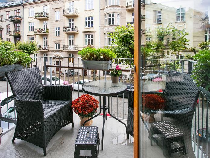 Mindre privat altan med to kurvestole og cafébord samt altankasser og blomster i krukker. Fra altanen er der udsigt til lyst, herskabeligt boligbyggeri.