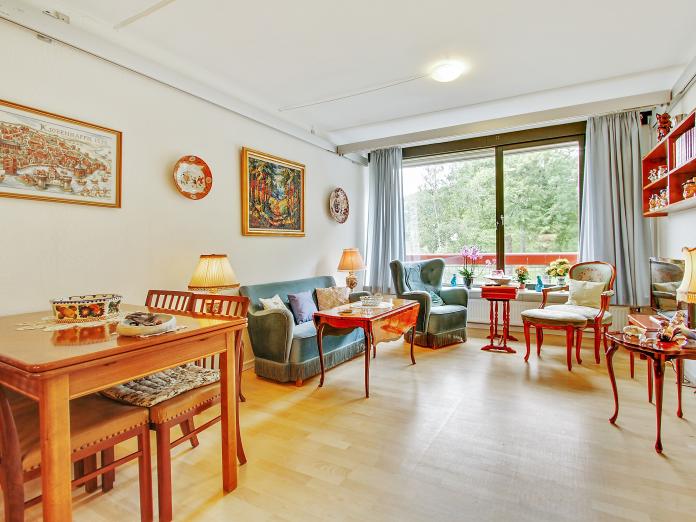 Lys stue med stort vinduesparti. Stuen er indrettet med sofa, lænestole og spisebord og -stole. 