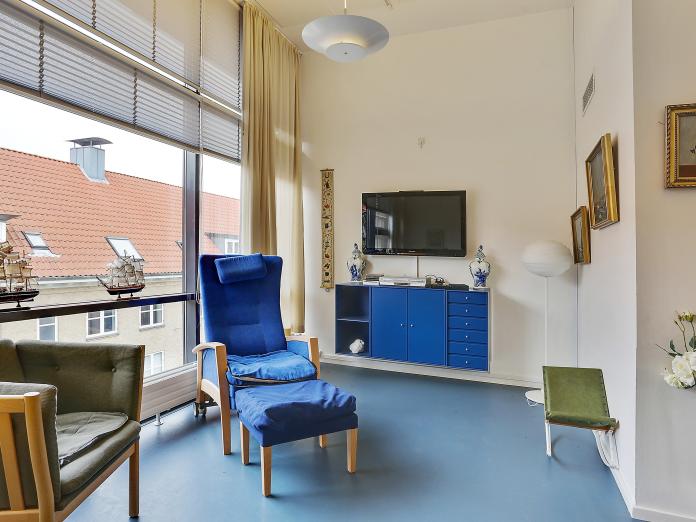 Fællesrum - et lille hjørne med en lænestol, sofa og tv på væggen og en lille skænk.