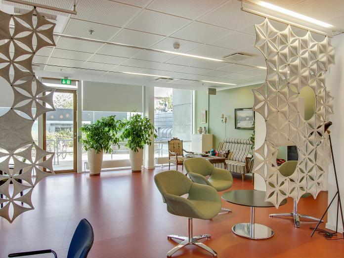 Fællesområde med lænestole, planter og vægkunst, der deler rummet lidt op.