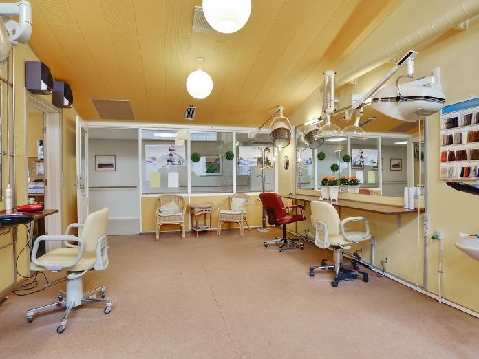 Rum indrettet som frisørsalon anno 1960 med lysegule vægge, tre frisørpladser med spejle og tørrehjelme. 