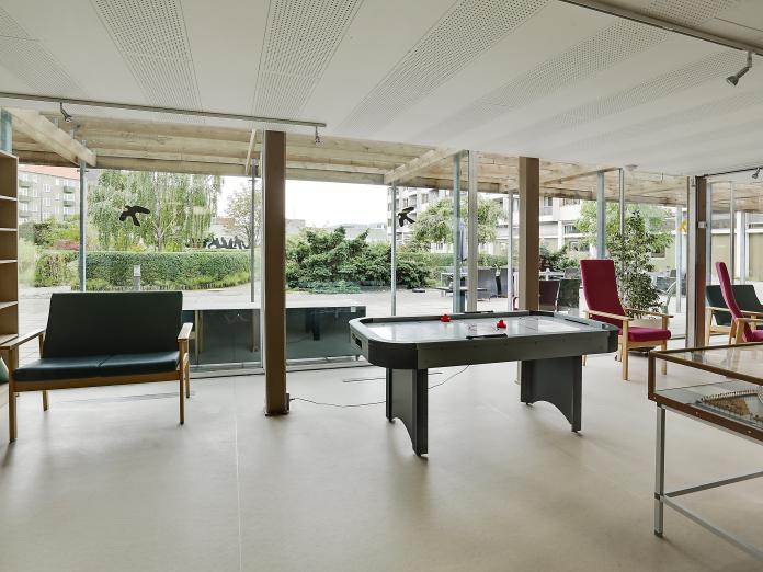 Fællesområde med store vinduespartier ud med gård. Rummet er indrettet med sofaer, lænestole og airhockeybord.