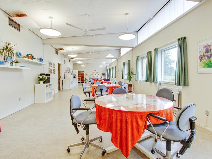 Aflangt, lyst aktivitetsrum indrettet med fire runde bord med kontorstole omkring. 