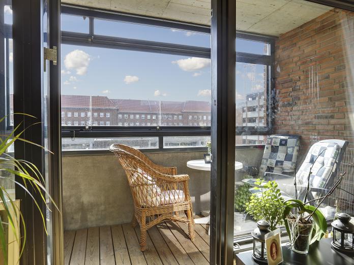 Overdækket altan med kig til blå himmel, træplanker og murstensvæg samt havestole og bord.