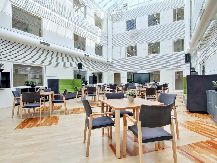 Stor, lys atriumgård med glastag. Rummet er indrettet med akustiksofaer og reoler langs væggene samt mange mindre borde med stole omkring.