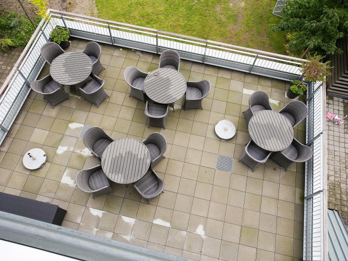 Kig til tagterrassen fra oven. Fire runde haveborde med stole. 