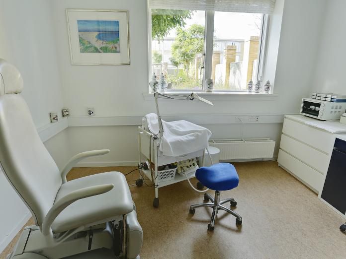 Rum indrettet til fodterapi med behandlingsstol, rullebord med redskaber samt taburet til behandleren.