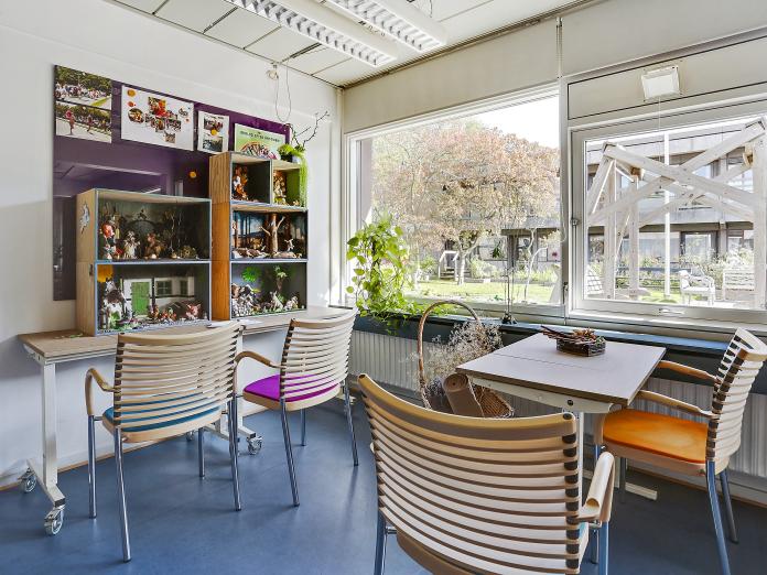 Hyggekrog med store vinduer ud mod gårdhave. Krogen er indrettet med cafébord og stole samt et bord med udstillingskasser med opstillinger af dyr om miljø fra fx en bondegård og en skov.