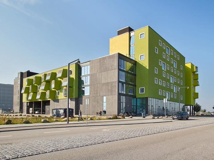 Moderne bygning i grå og grønne farver med hvide vinduer og altaner set fra vejen.