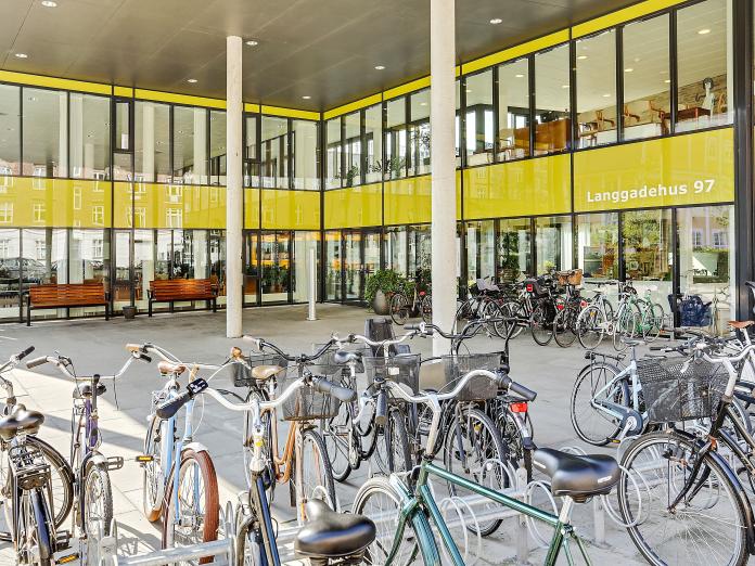 Overdækket indgangsareal med cykelstativer med cykler og bænke.