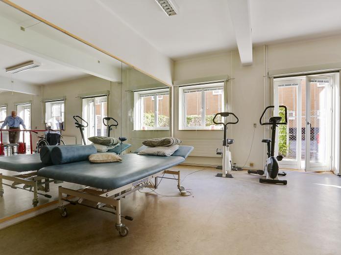 Motionsrum med terrassedør ud til gårdhave. Rummet er indrettet med kondicykler, gangbarre og en behandlingsbriks.