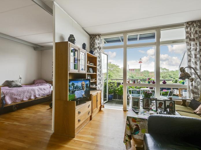 Kig fra stue ind i soveværelse. Fra stuen er der en dør du til altan med blomster i krukker.