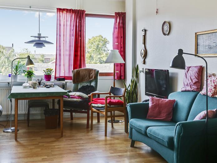 Lys stue med store vinduespartier. Stuen er indrettet med personlige møbler som sofa, bord og stole samt fjernsyn, standerlampe, fjernsyn og malerier.