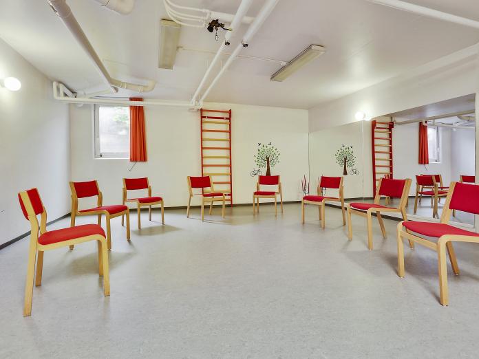 Træningssal med stole og ribbe på bagvæggen. Den ene væg er beklædt med spejle fra gulv til loft.