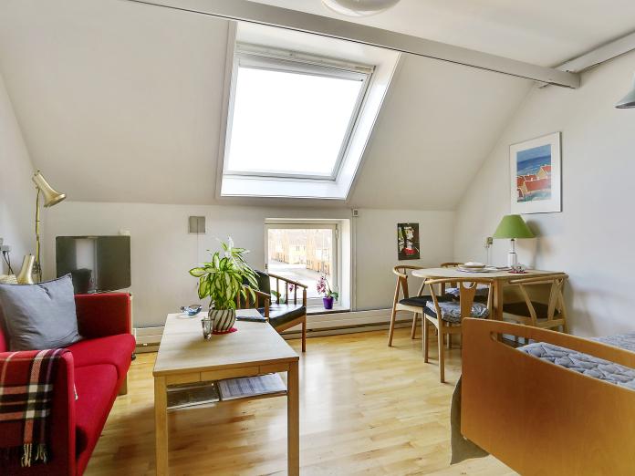 Lyst værelse med plejeseng, loftslift og ovenlysvindue. Værelset er indrettet med sofa, sofabord, lænestol samt stole omkring et spisebord.