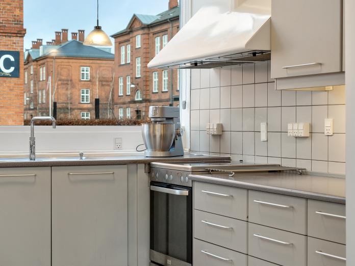 Fælles køkken i hvide elementer. Fra køkkenvinduet er der kig til røde murstenbyggeri af ældre dato.